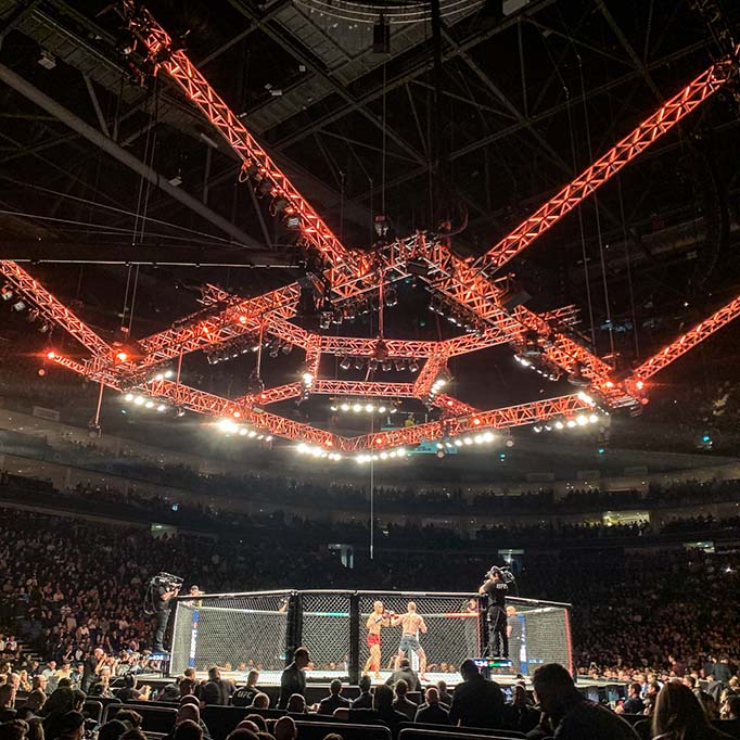 A lighting rig set above a fighting cage, with two wrestlers inside the octagon fight cage