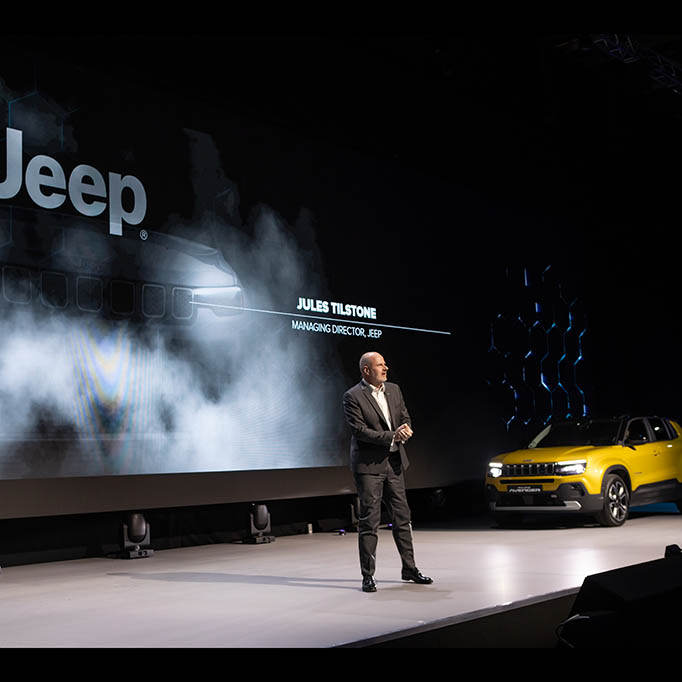 Man on a stage with a jeep entering, beautifully lit.